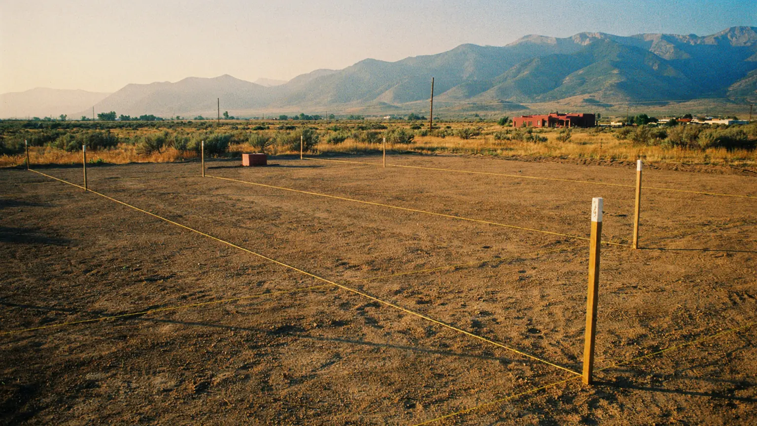 A bare high-desert lot at dawn, with string lines and stakes marking future landscape beds